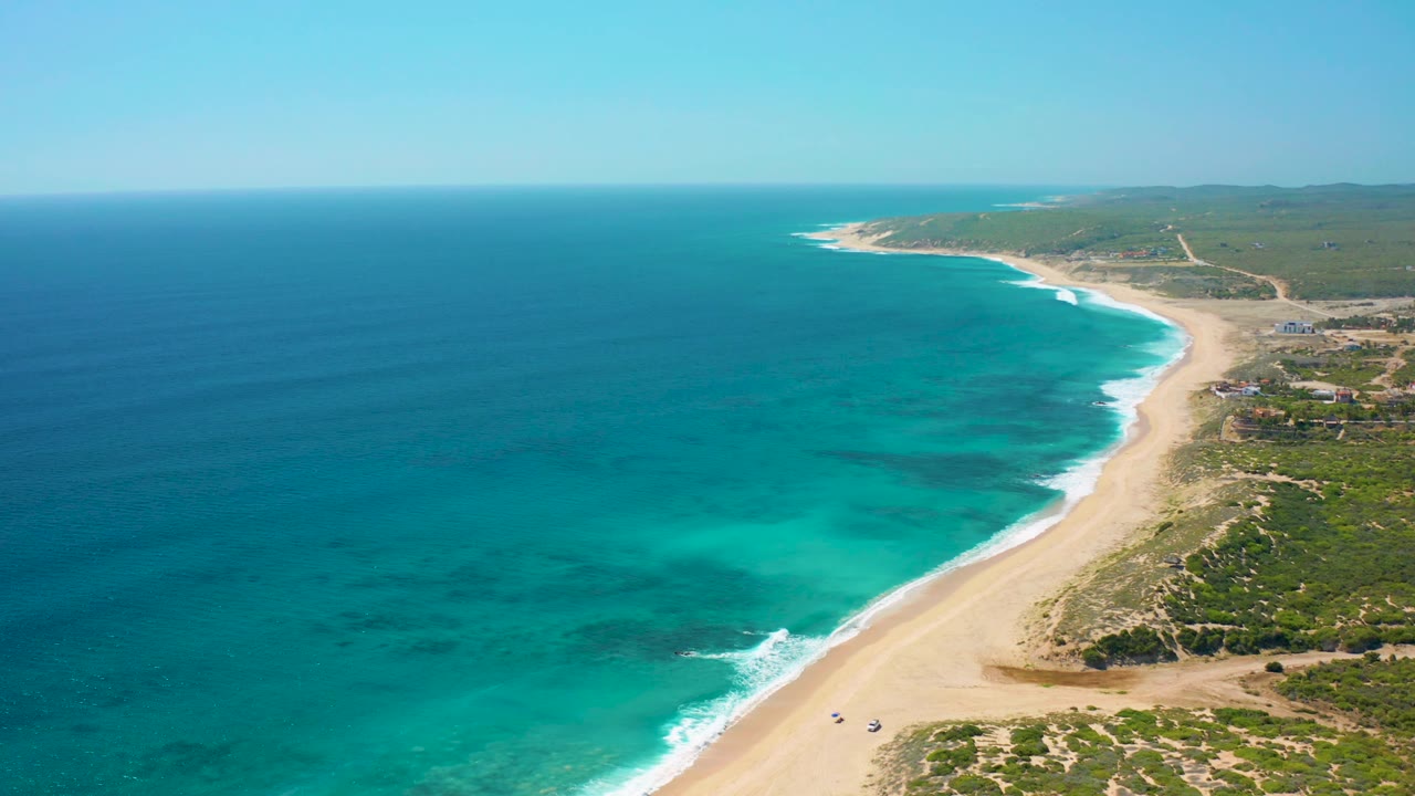 High aerial view of turquoise sea, pale sand, and green coastal terrain.