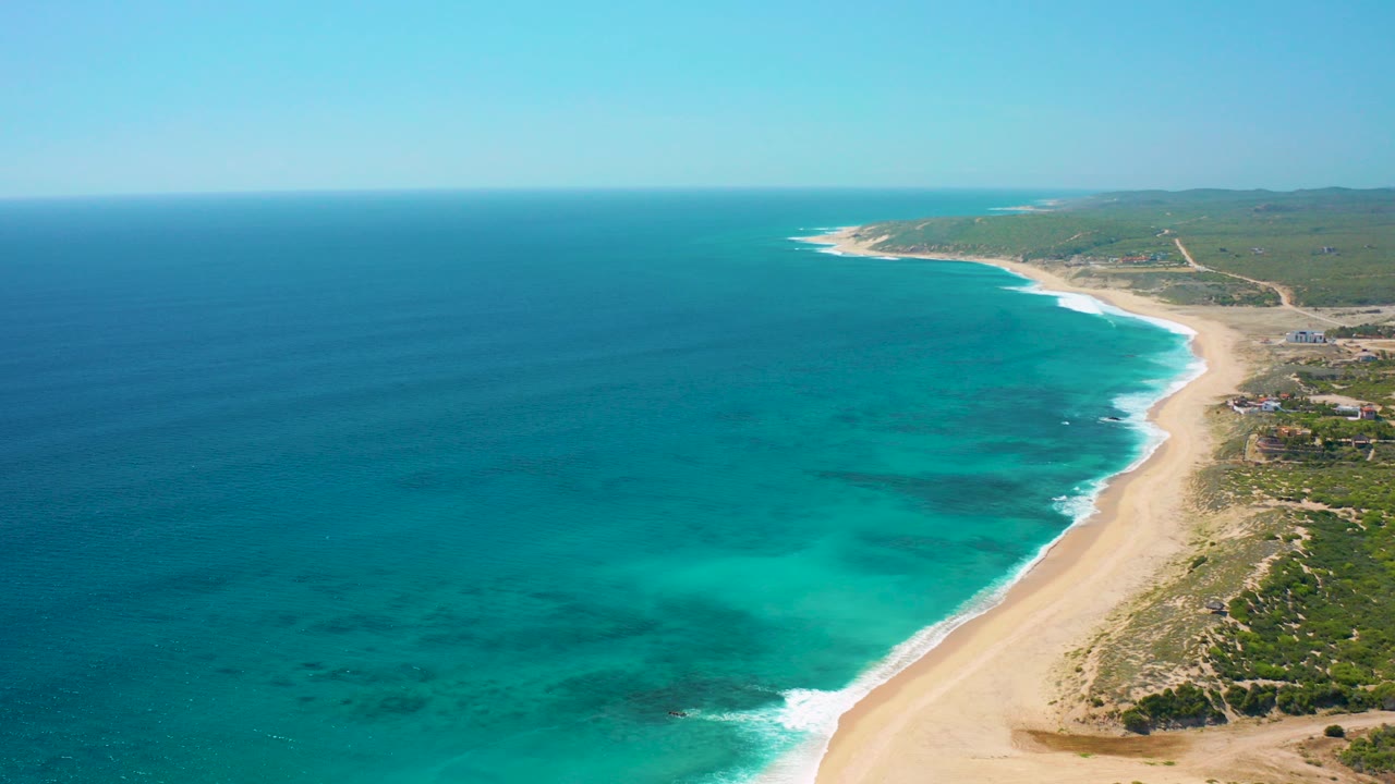Aerial view of turquoise sea beside a sandy coastline and low green land.