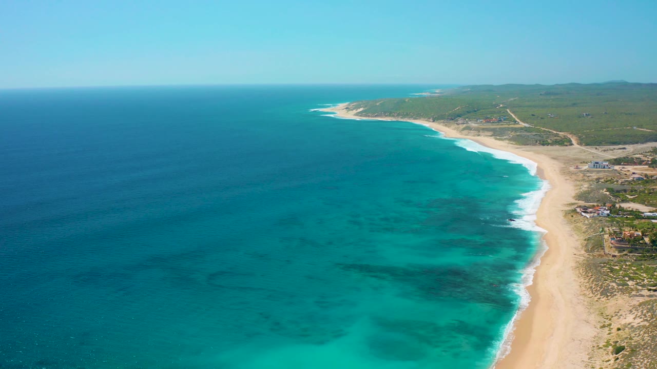 Aerial view along a quiet beach with blue ocean filling the left side.