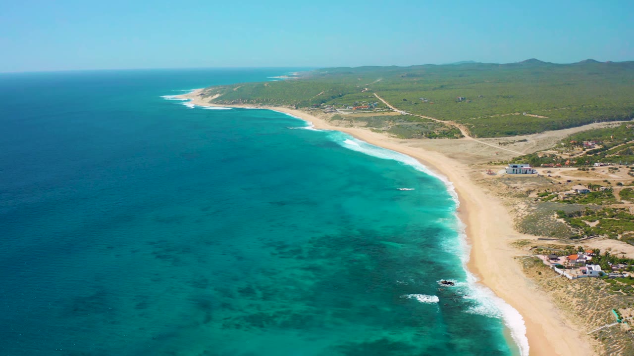 Drone view of blue-green water and a curved sandy shore.