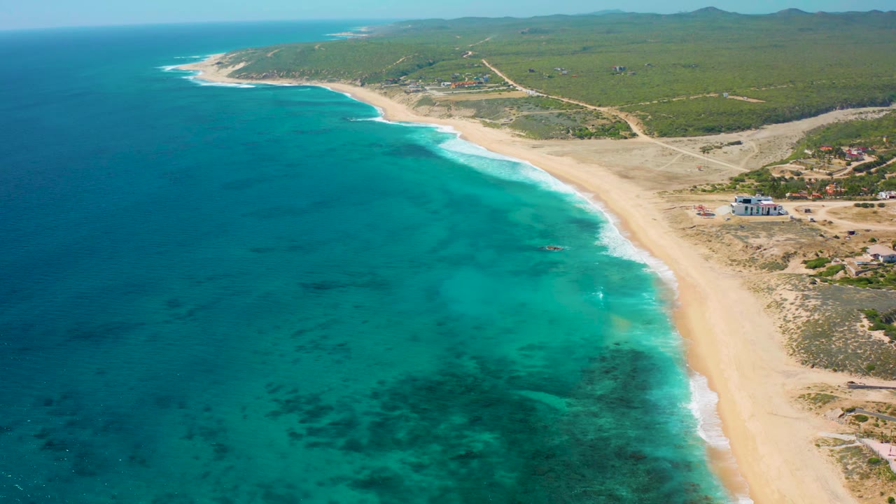 Aerial coastline frame with turquoise water in the foreground and sand curving along inland scrub.