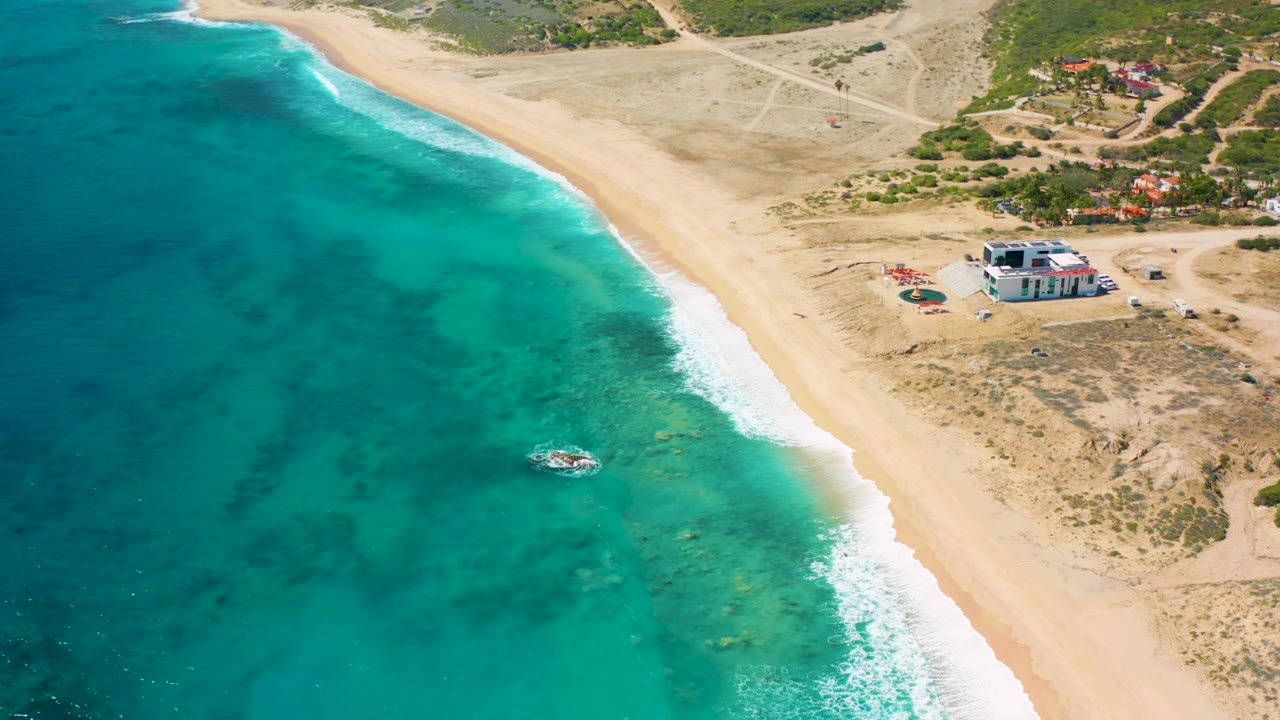 Drone view of clear green-blue water, beach, small boat, and dry coastal land.