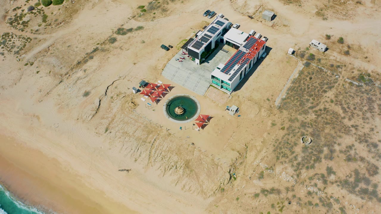 Aerial beach view with surf entering the lower corner near a modern structure.