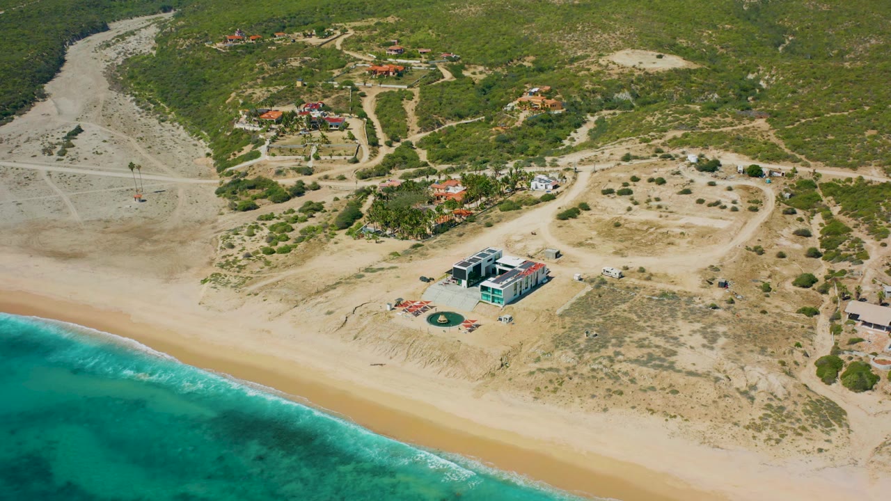 High aerial of beach water, sandy shoreline, beachfront house, access roads, and vegetation.
