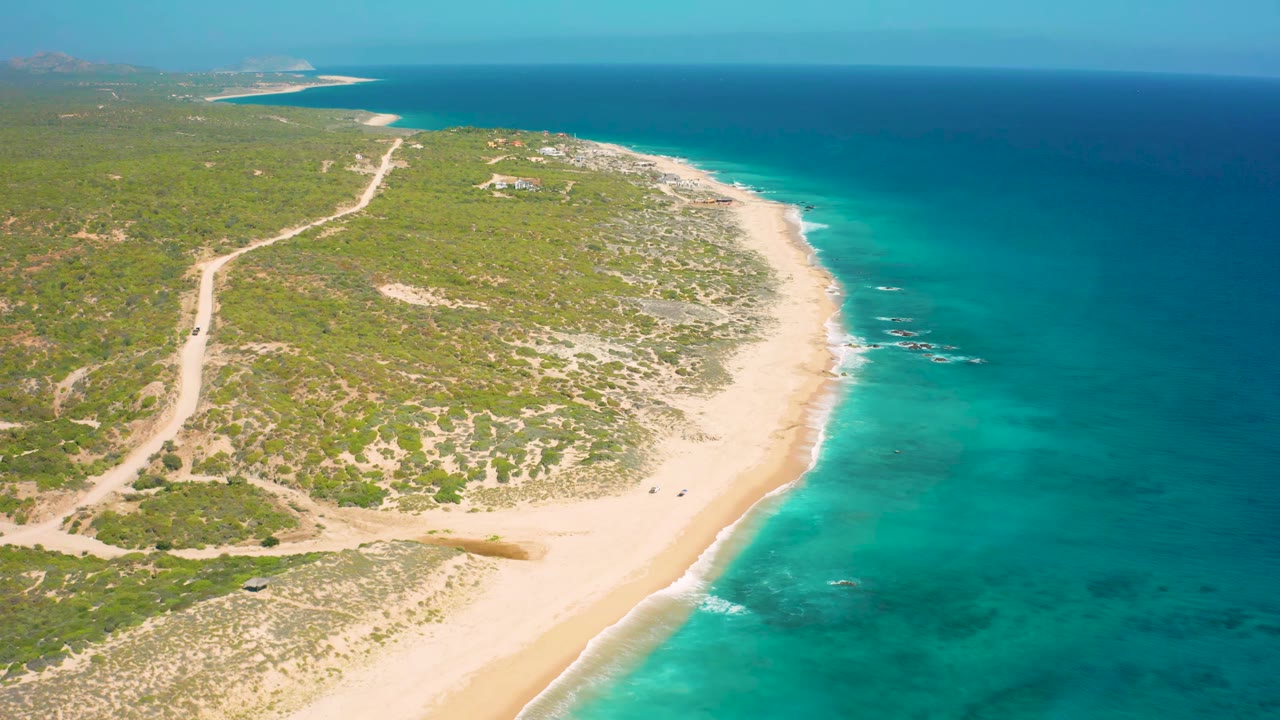 Drone view of curving beach beside clear blue water