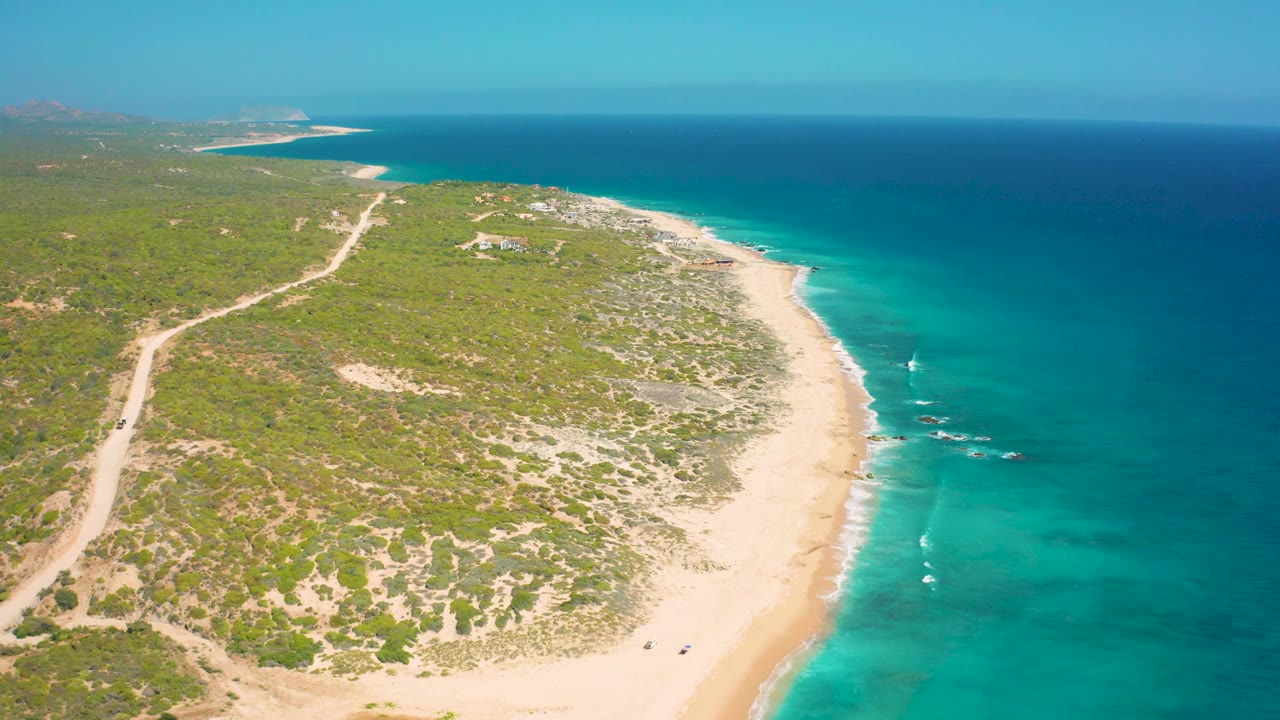 Coastal aerial view with a sandy beach curving beside clear blue water.