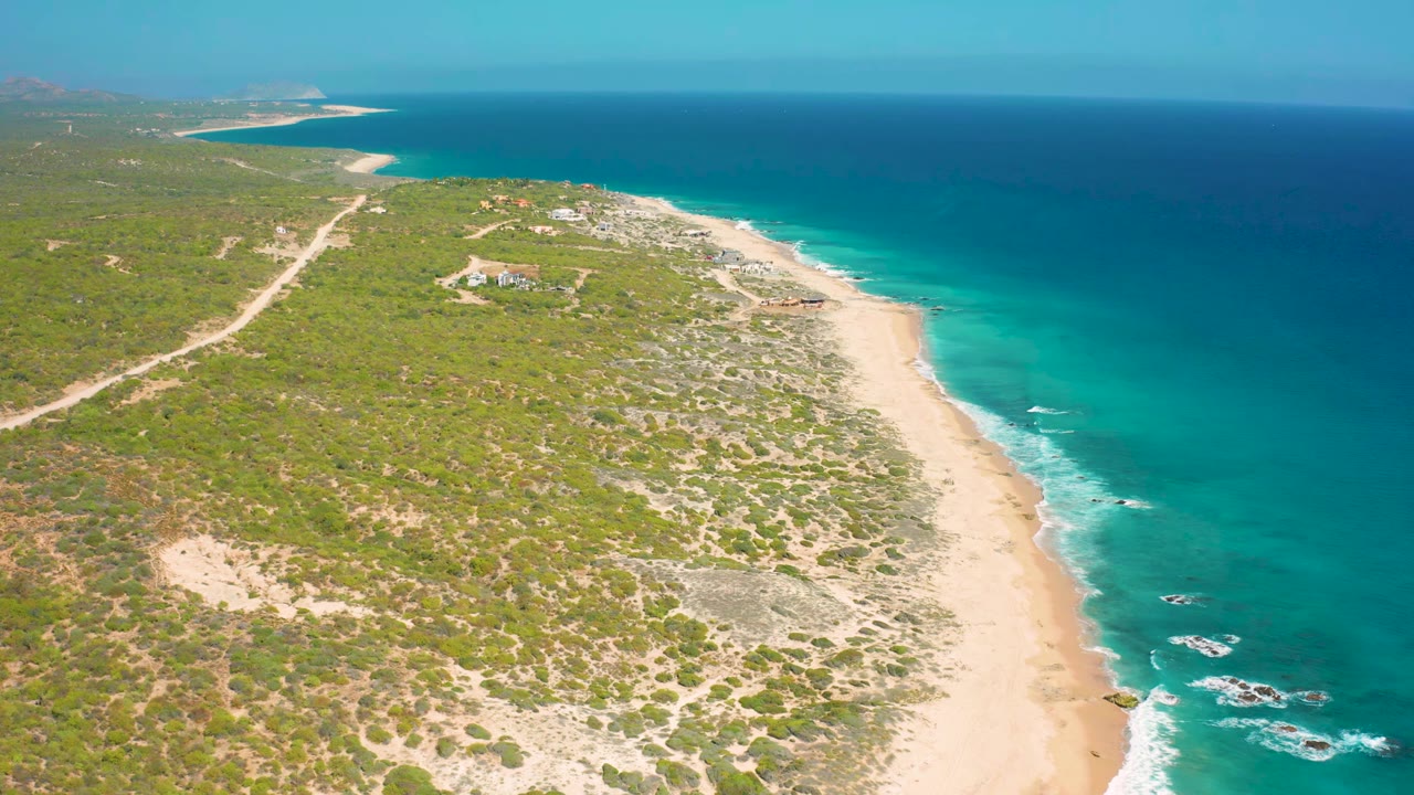 Elevated coastline view with dirt road through scrub and turquoise surf along a sandy beach.