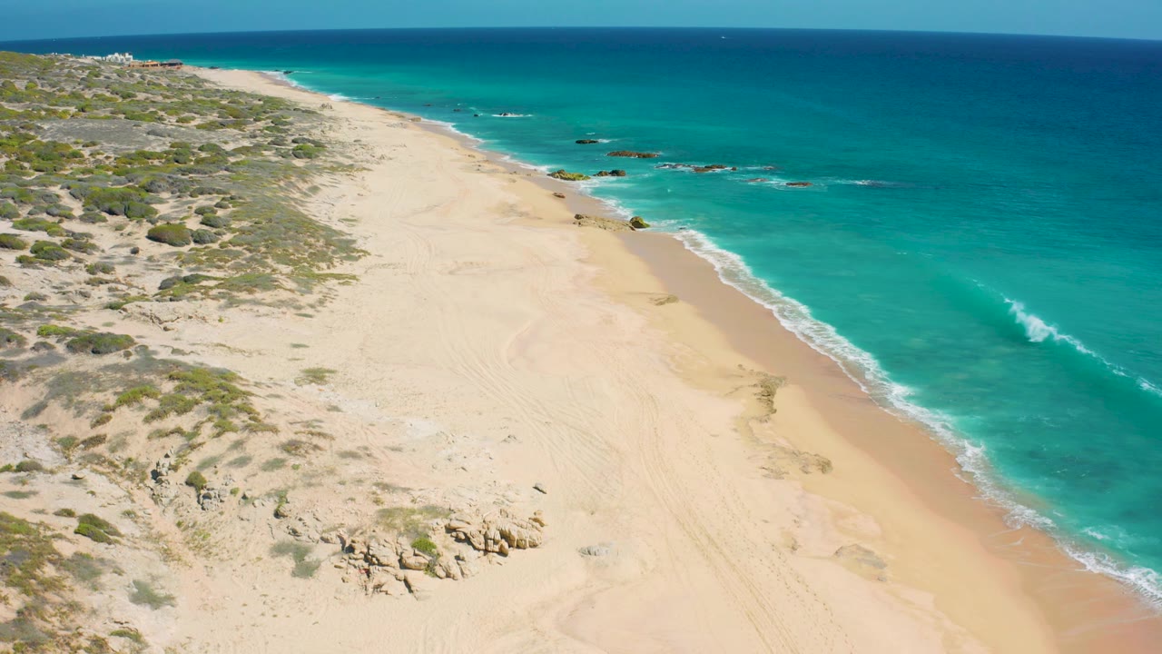 Aerial coastline with scrub dunes, empty sand, and mild waves.
