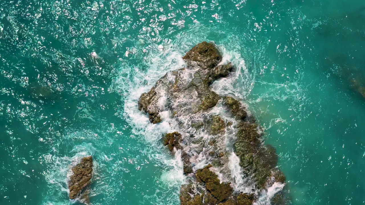 Overhead turquoise ocean water breaking around algae-covered rocks.