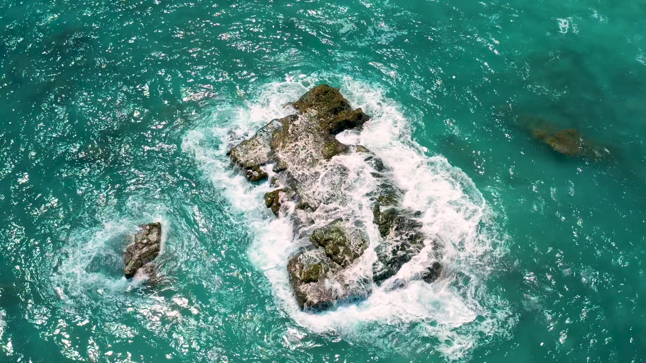 Overhead turquoise ocean with white surf around two rock outcroppings.