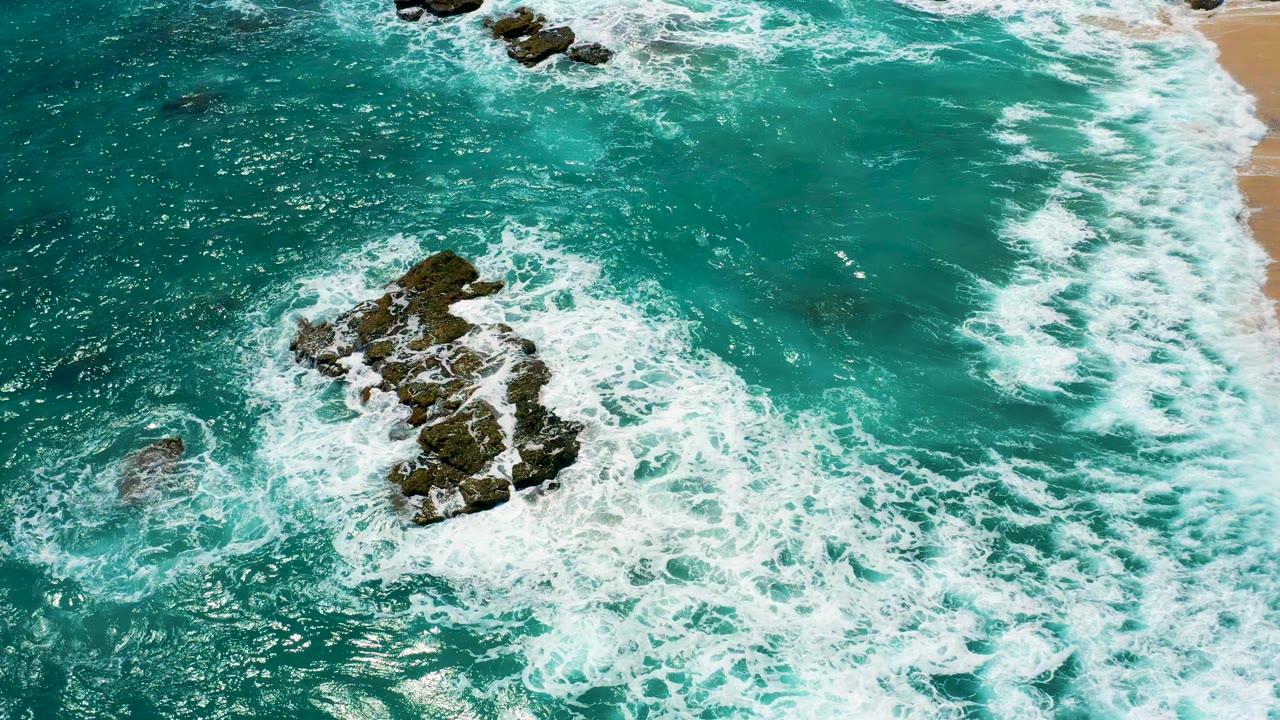 Overhead turquoise surf around dark coastal rocks