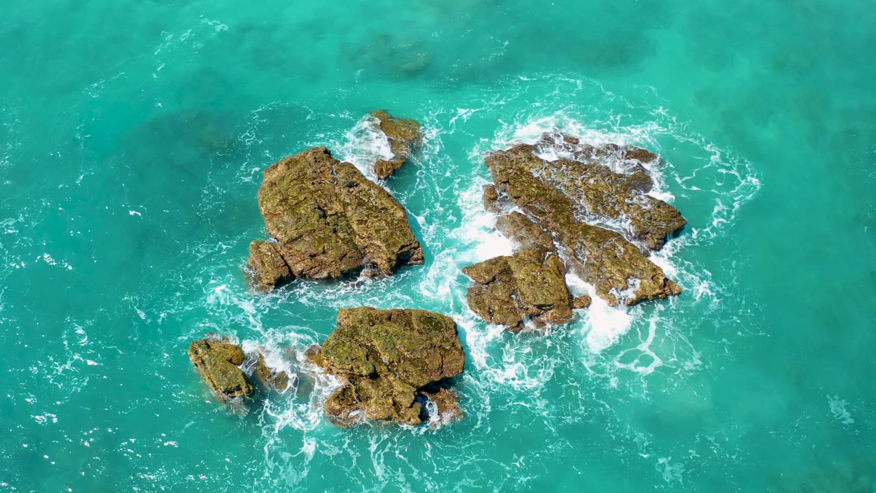 Turquoise sea with brown rocks and foam spreading between outcrops