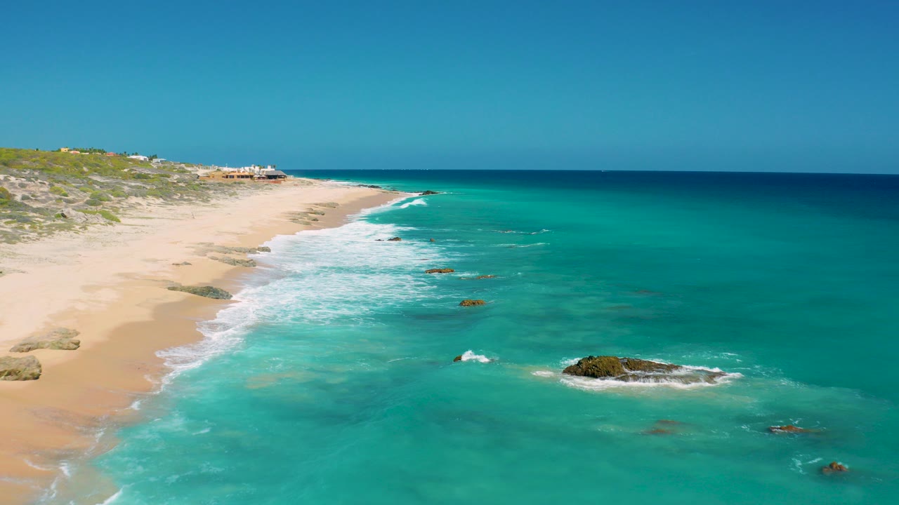 Aerial view of sandy beach, turquoise ocean, surf, and rocks.