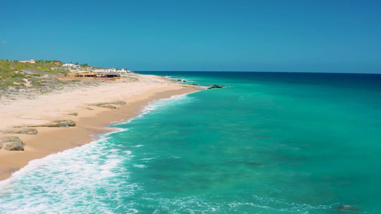 Aerial coastline with foamy waves reaching a quiet sandy beach