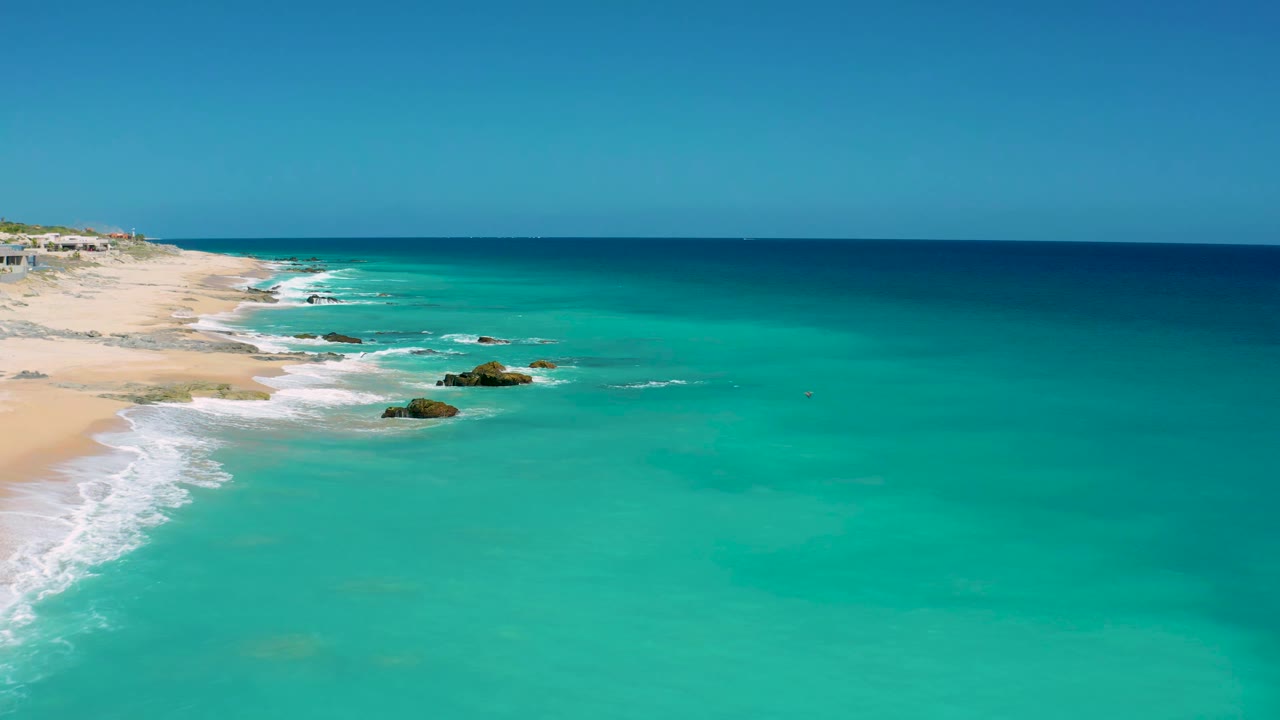 Wide aerial coast with clear water, surf, and rocks near shore.