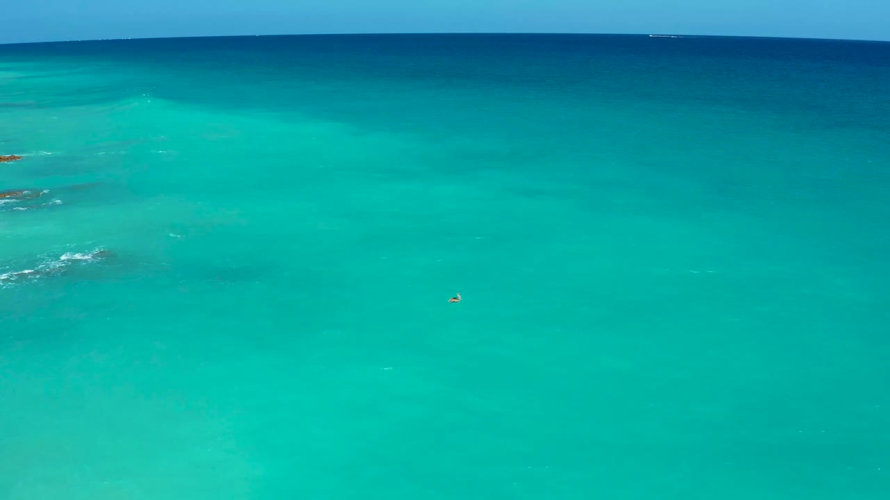 Clear teal water with faint submerged patches and a tiny object near center.