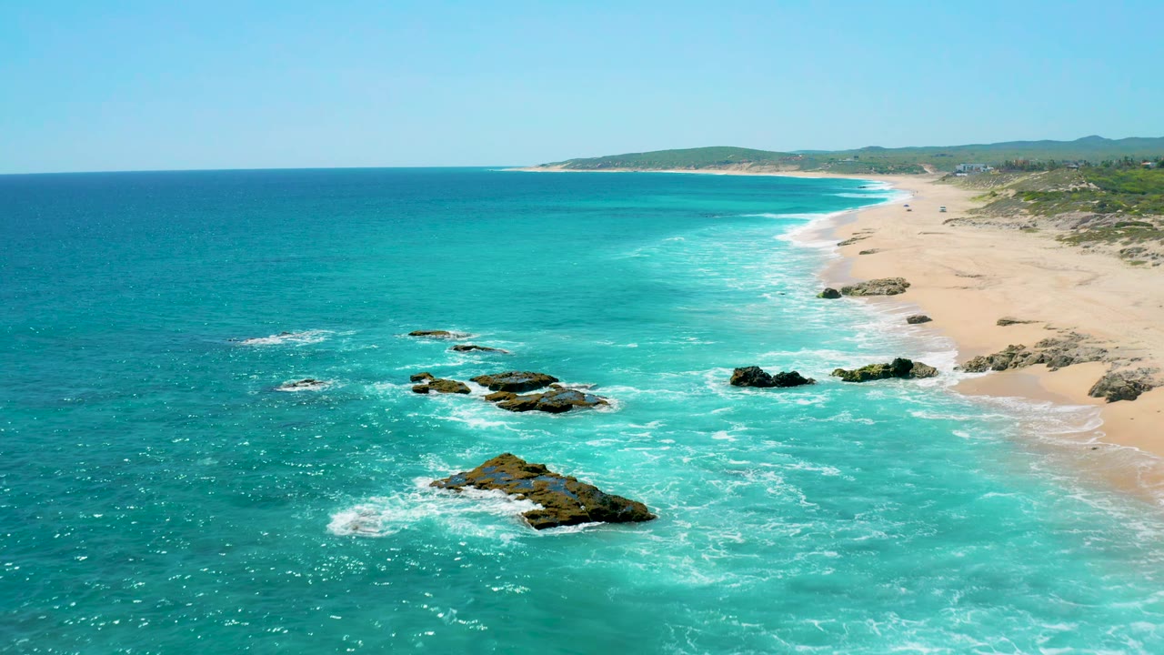 Drone view of shallow blue water and rocks beside a sandy shoreline