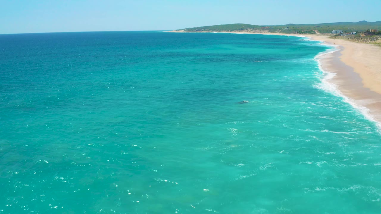 Aerial beach view with shallow turquoise water and surf along the sand.