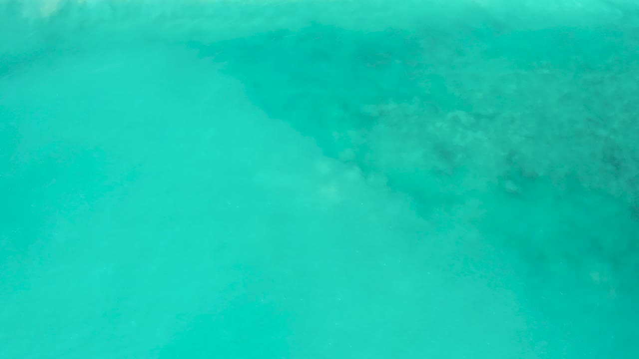 Clear blue water over pale sand and dark underwater patches.