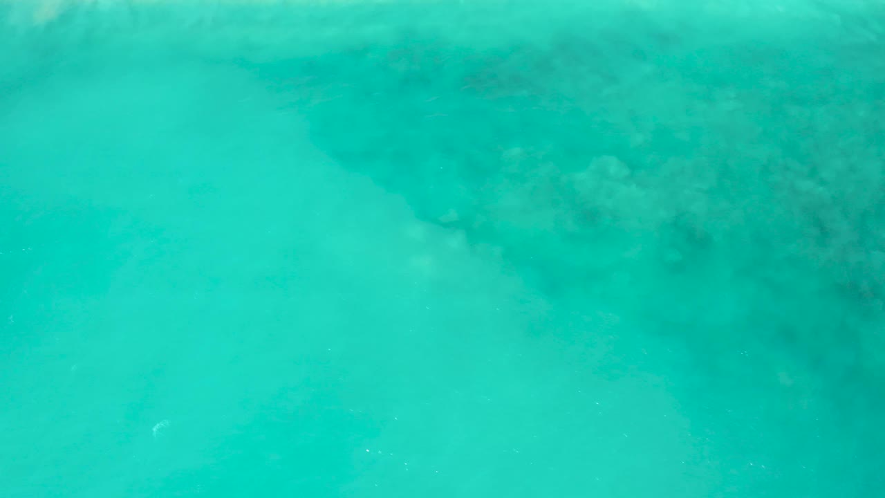 Bright turquoise water in El Cardoncito, Baja California Sur, showing soft wave haze over darker submerged shapes and no visible people.