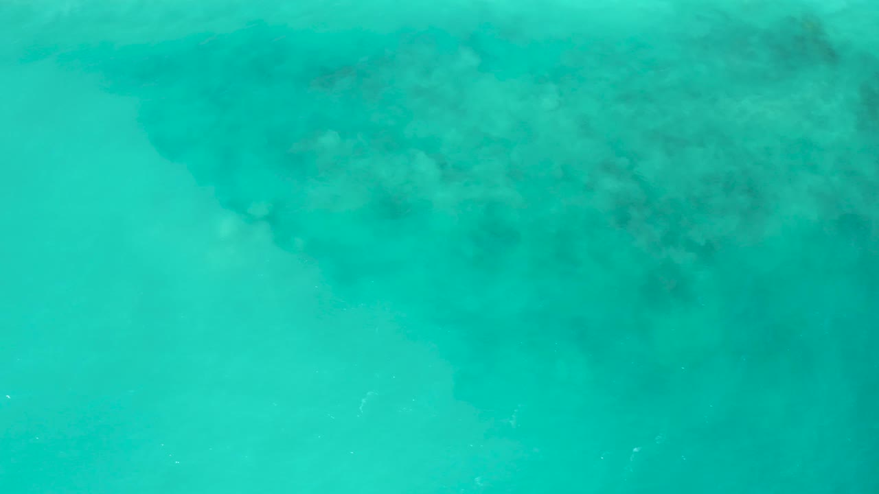 A nearly top-down frame of shallow turquoise sea at El Cardoncito shows mottled darker underwater patches along the top edge and no visible people.