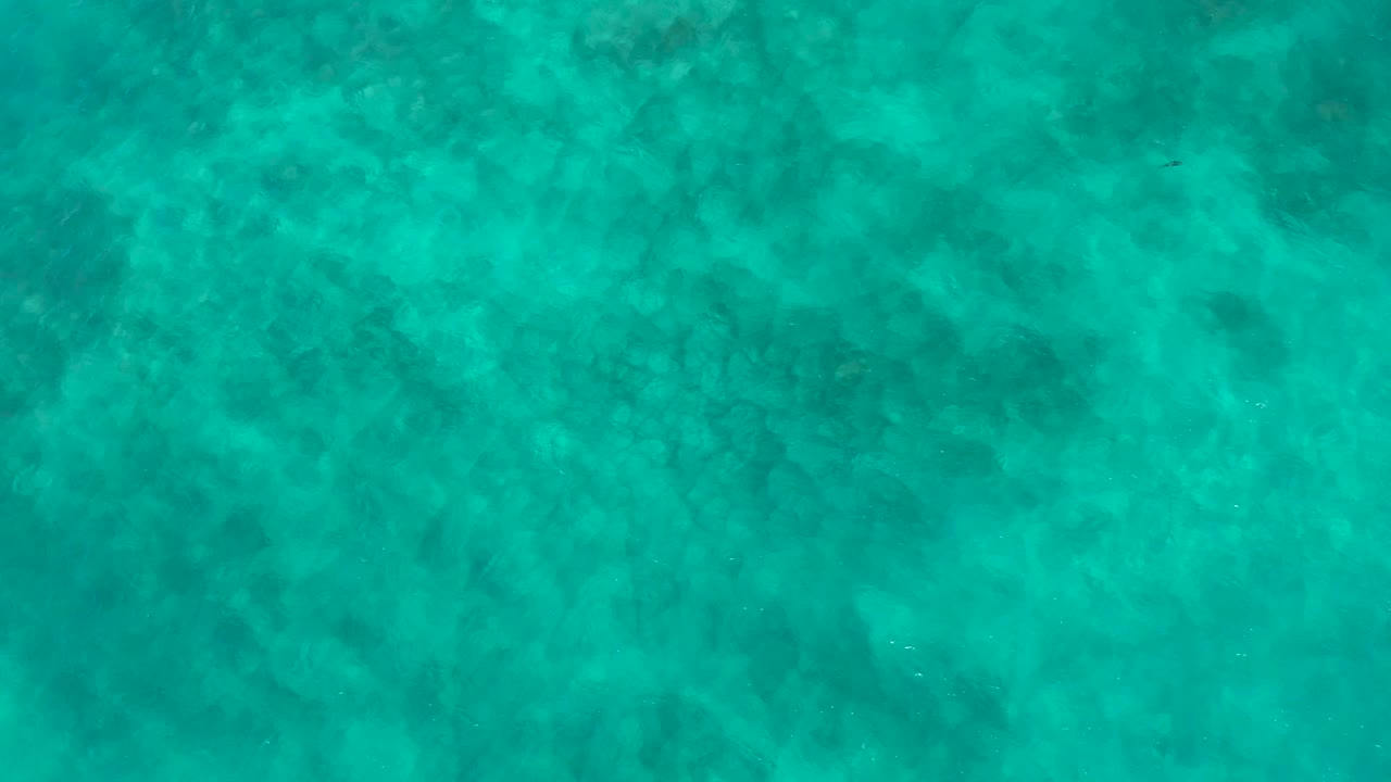 Aerial frame of blue-green ocean water at El Cardoncito with a softly mottled bottom pattern and no visible people.