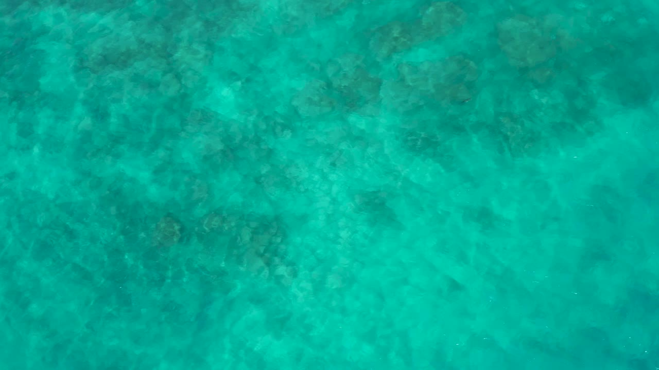 Clear blue-green sea water fills the frame at El Cardoncito, with mottled underwater patterns visible beneath the surface and no visible people.