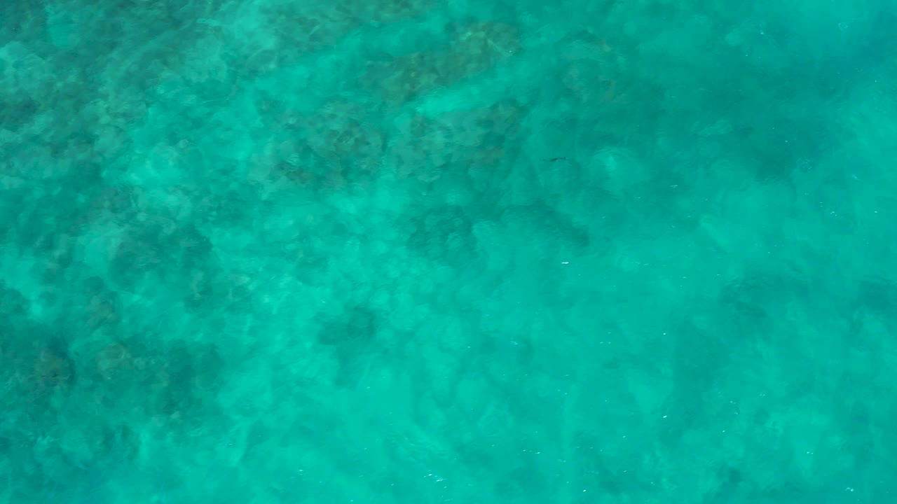 Turquoise ocean surface at El Cardoncito covers darker reef-like patches beneath the water, with no shoreline, vessels, or visible people in frame.