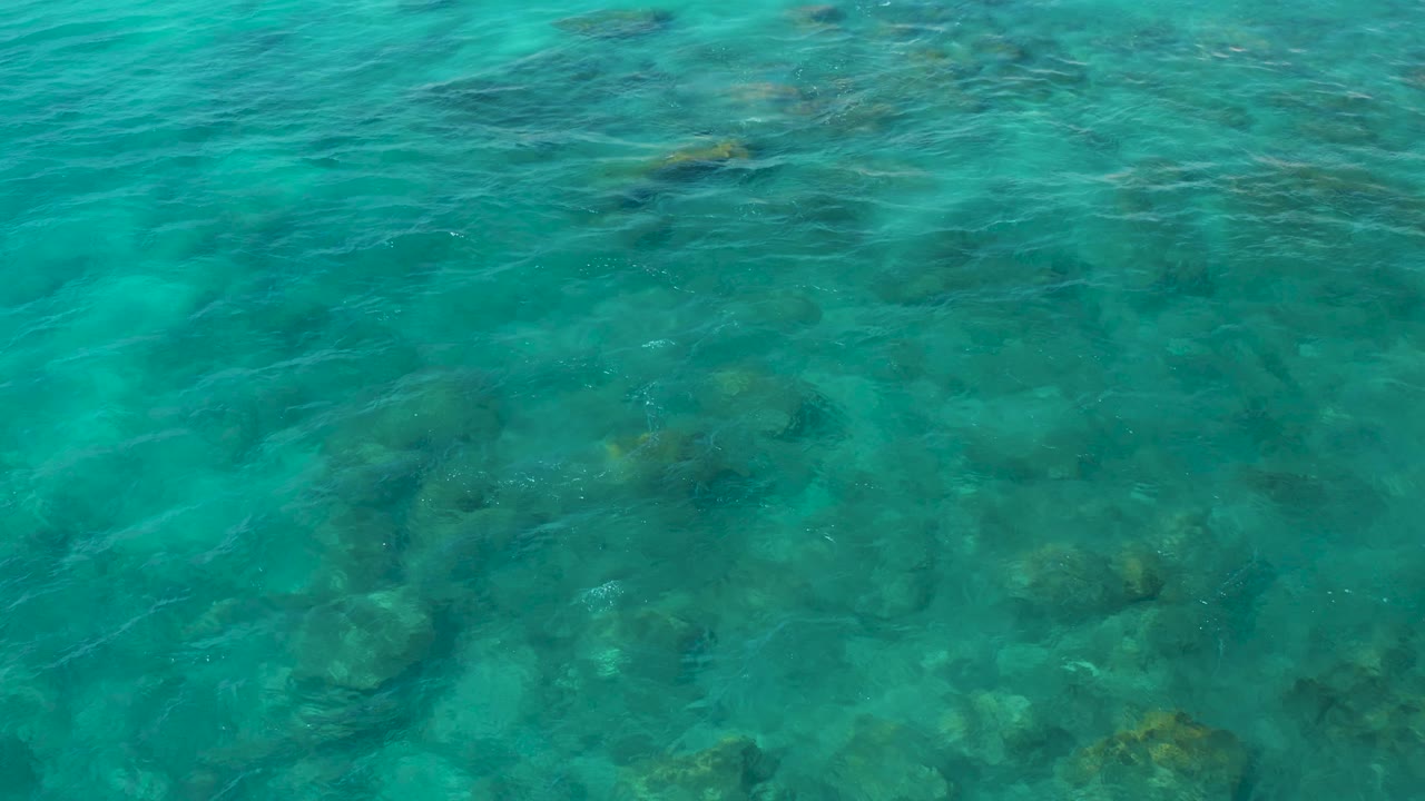 Shallow turquoise ocean water fills the frame, with uneven rock shapes visible under the surface at El Cardoncito and no visible people.