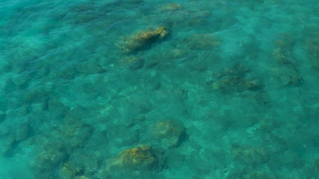 A high overhead view at El Cardoncito shows turquoise water, darker rock shapes below, and no visible people or vessels.