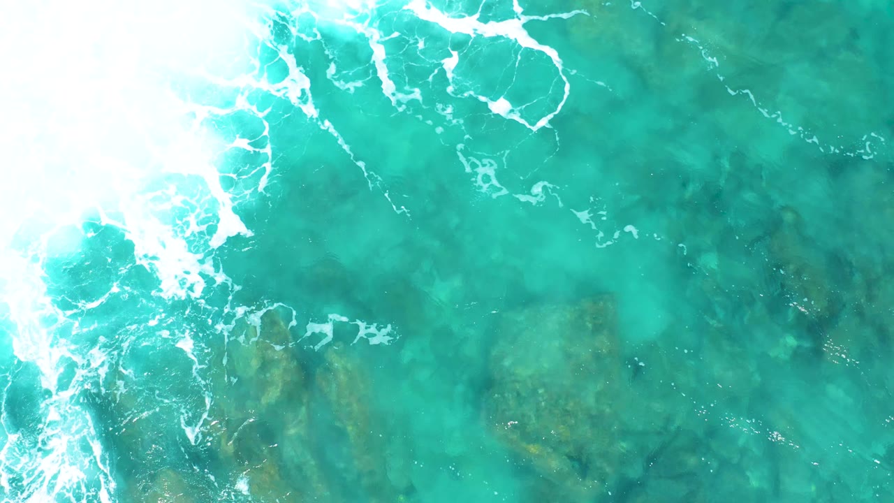 Clear aqua water with foam lines and underwater rock shapes.