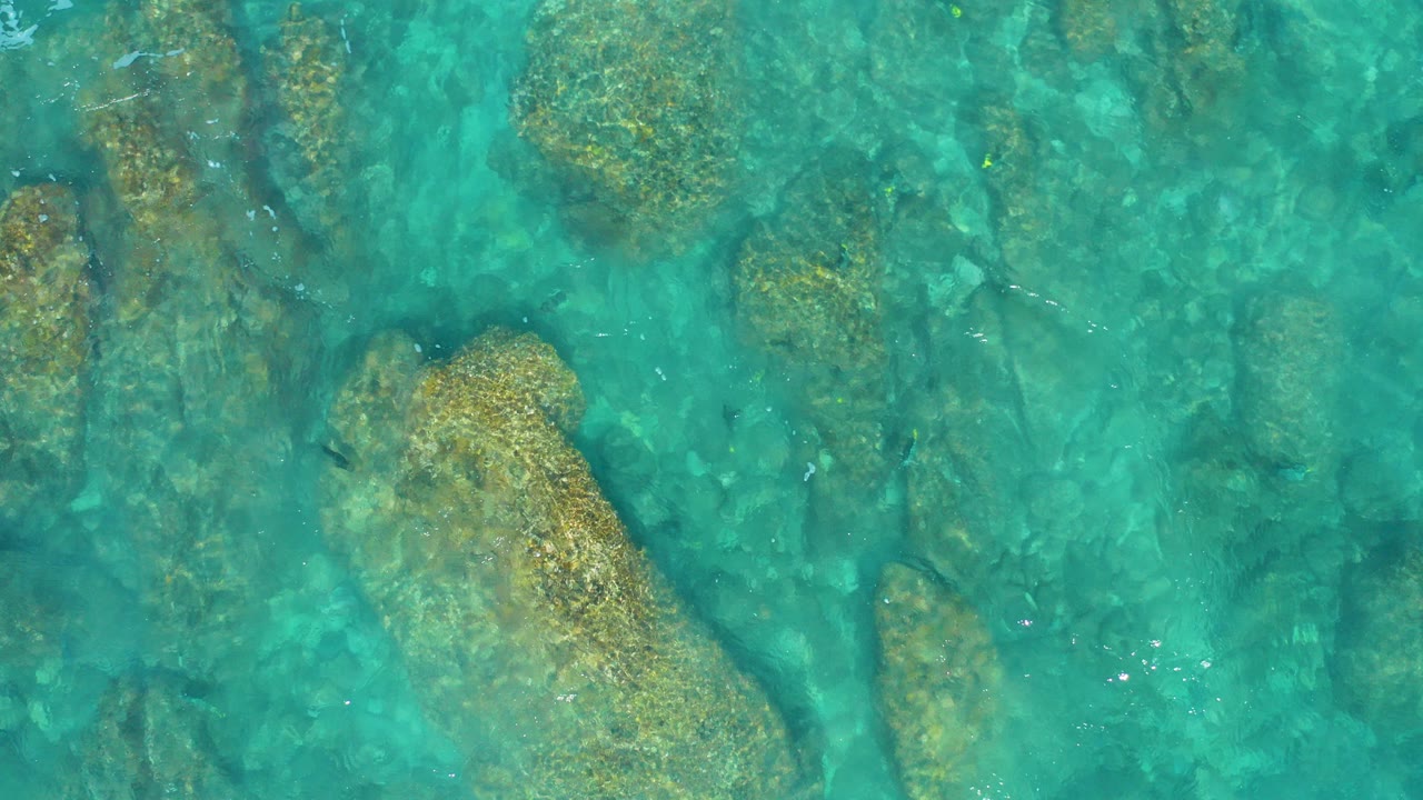 Overhead view of turquoise water washing across submerged tan rocks in El Cardoncito, Baja California Sur, with no visible people.