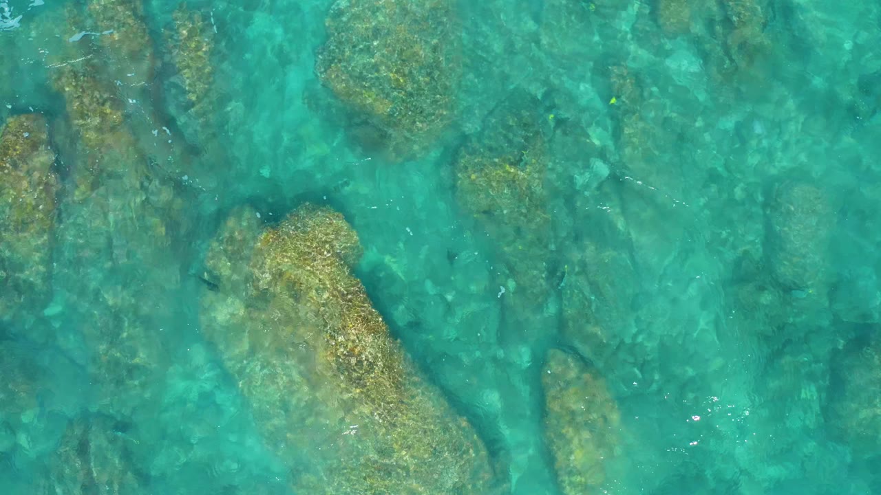 Blue-green seawater covers a cluster of submerged rocks in El Cardoncito, Baja California Sur, with faint ripples and no visible people.