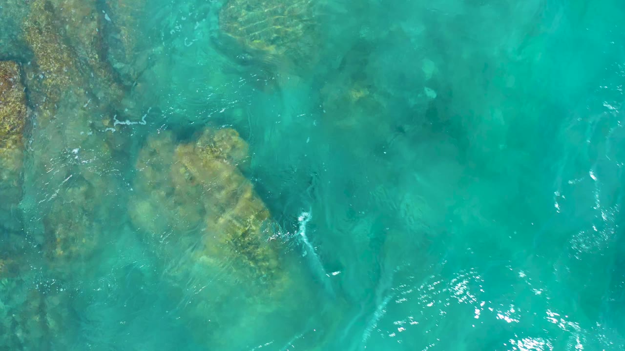 Clear blue-green water with tan rock forms below the surface.