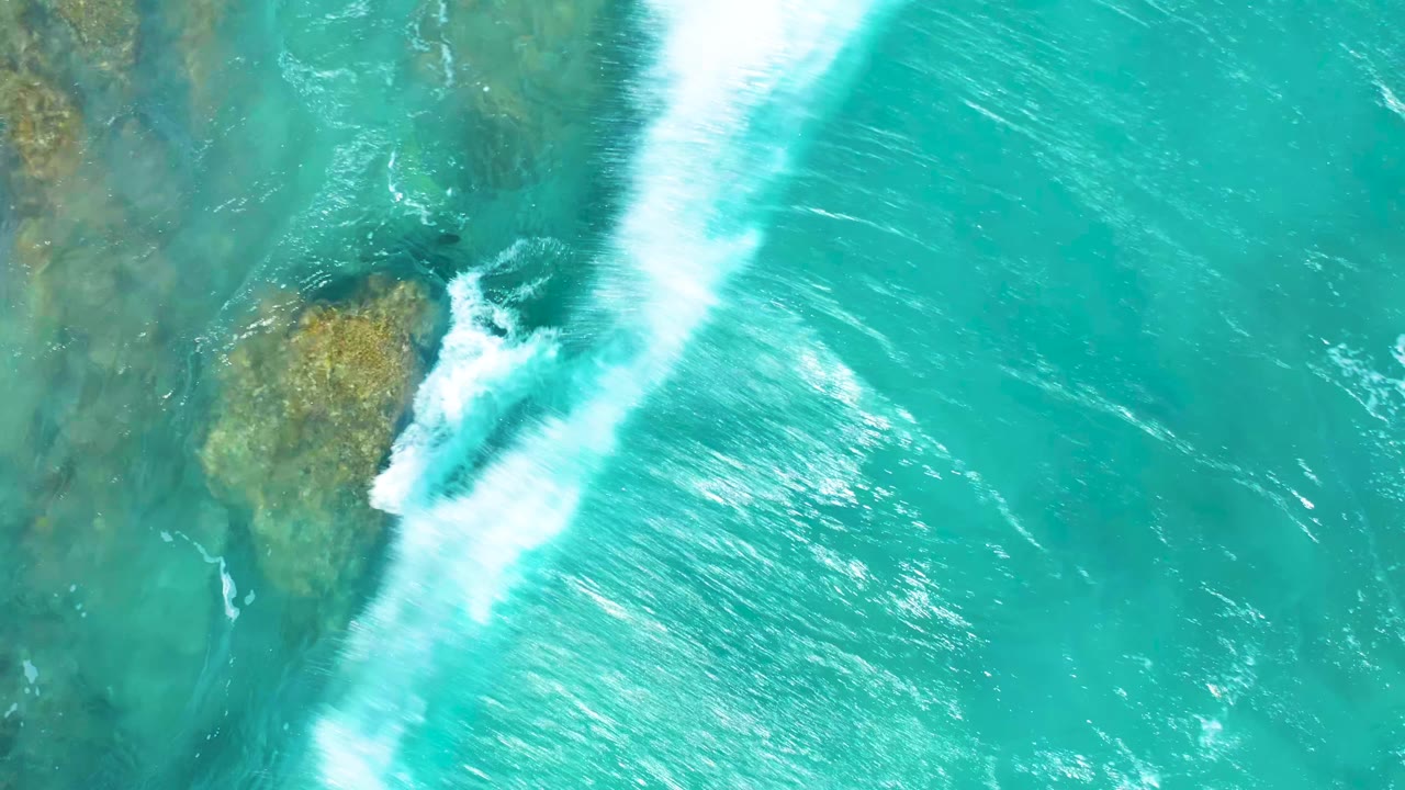 Foaming surf wrapping around shallow rocks in clear blue-green water