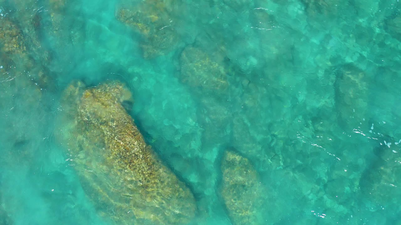 At El Cardoncito, clear teal water reveals submerged rocks near the left and center of frame, with no visible people or structures.