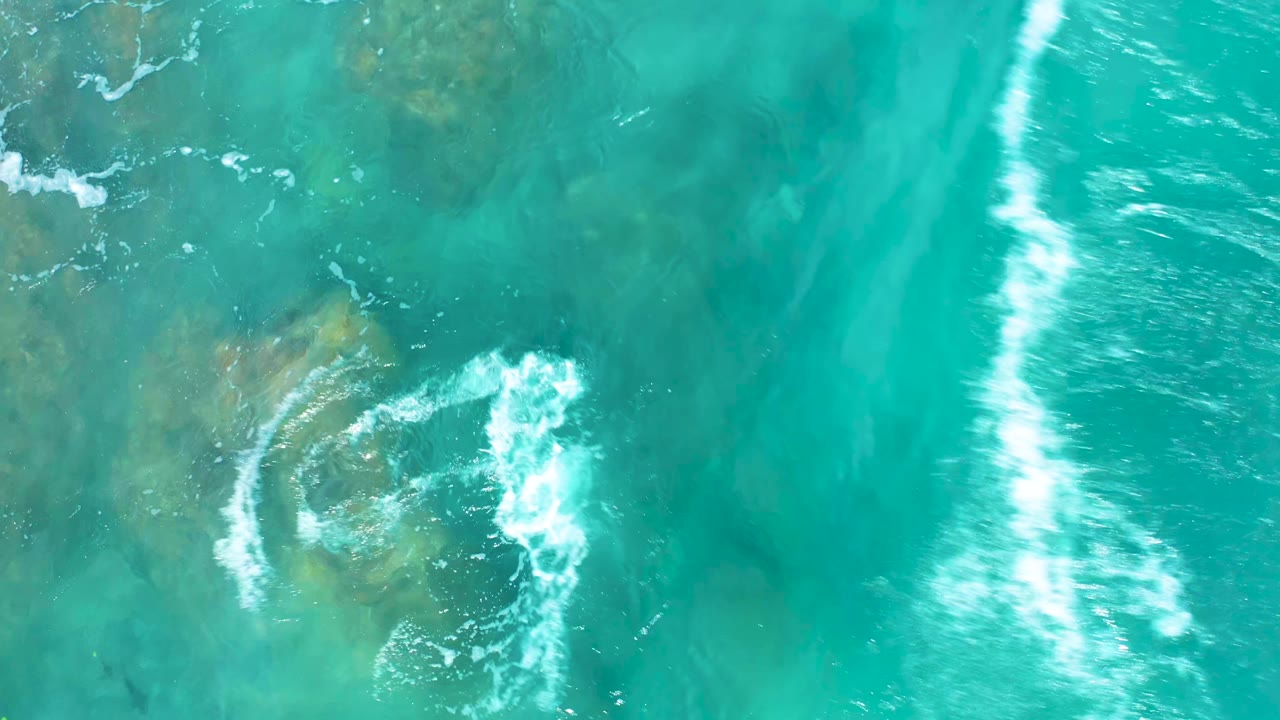 Turquoise shallows with foam breaking around a rock patch.