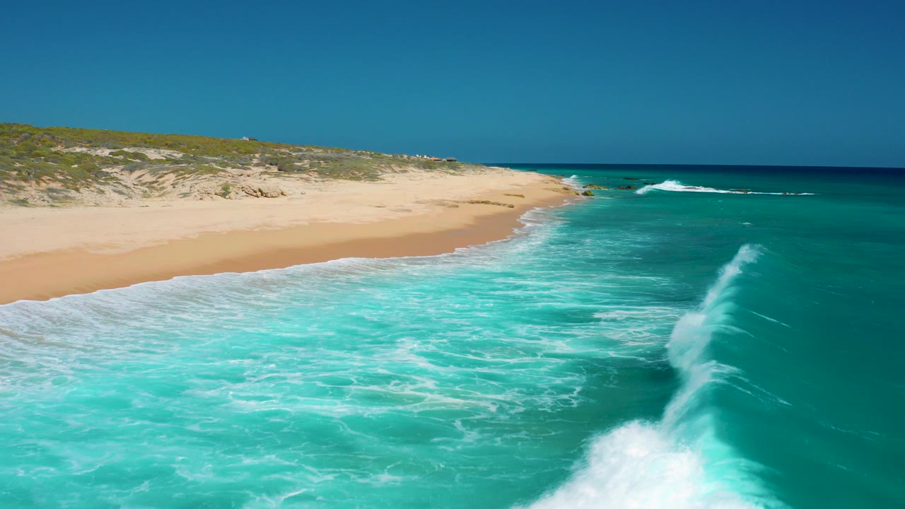 Aerial view of turquoise surf breaking beside a sandy beach