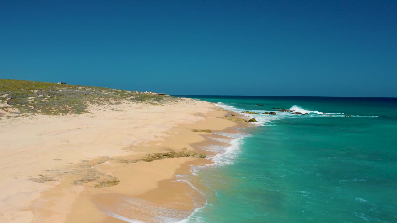 Aerial view of sandy beach and turquoise surf under a clear sky