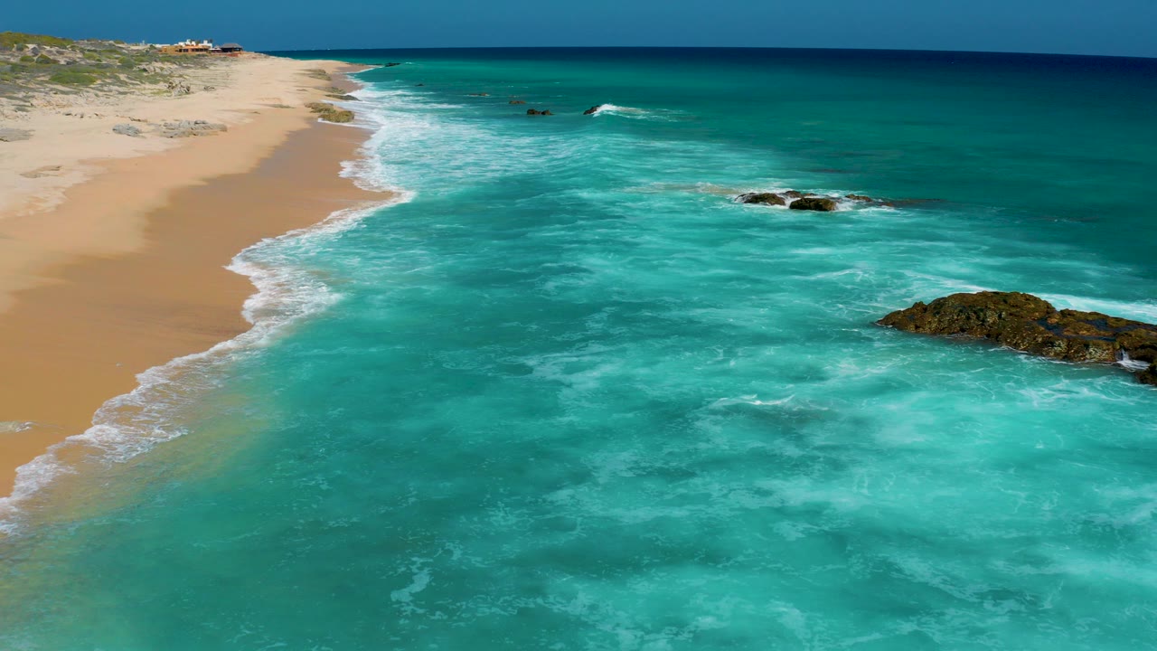 Aerial view of sandy beach, turquoise surf, and rocky outcrops.