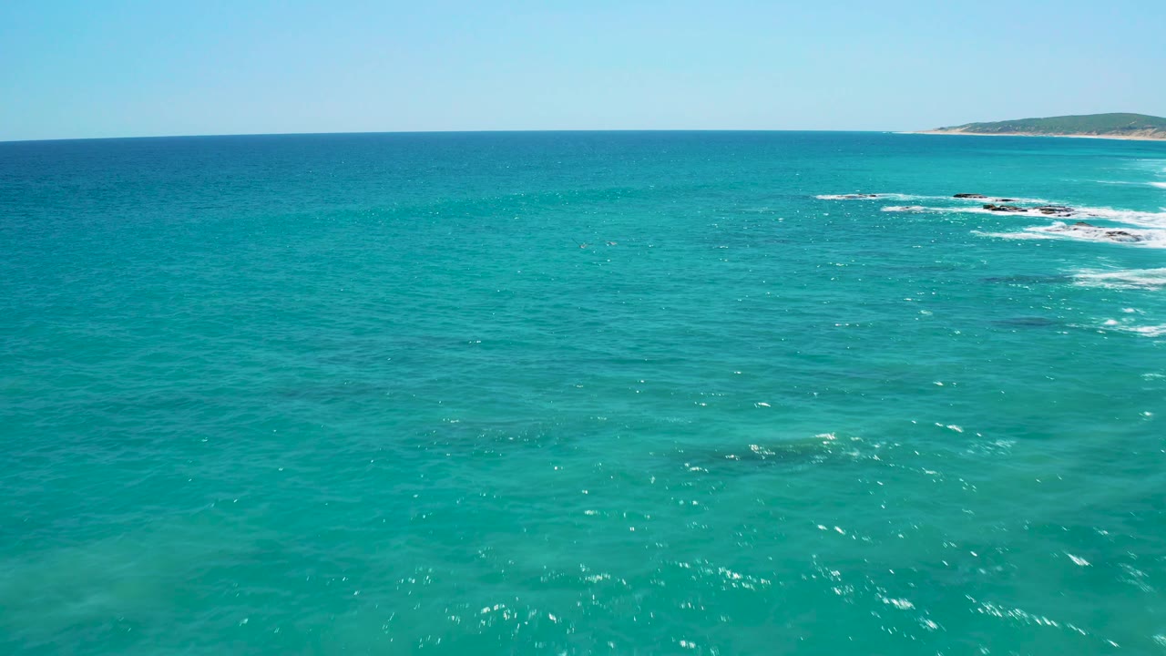 Turquoise ocean and low shoreline with white waves over rocks.