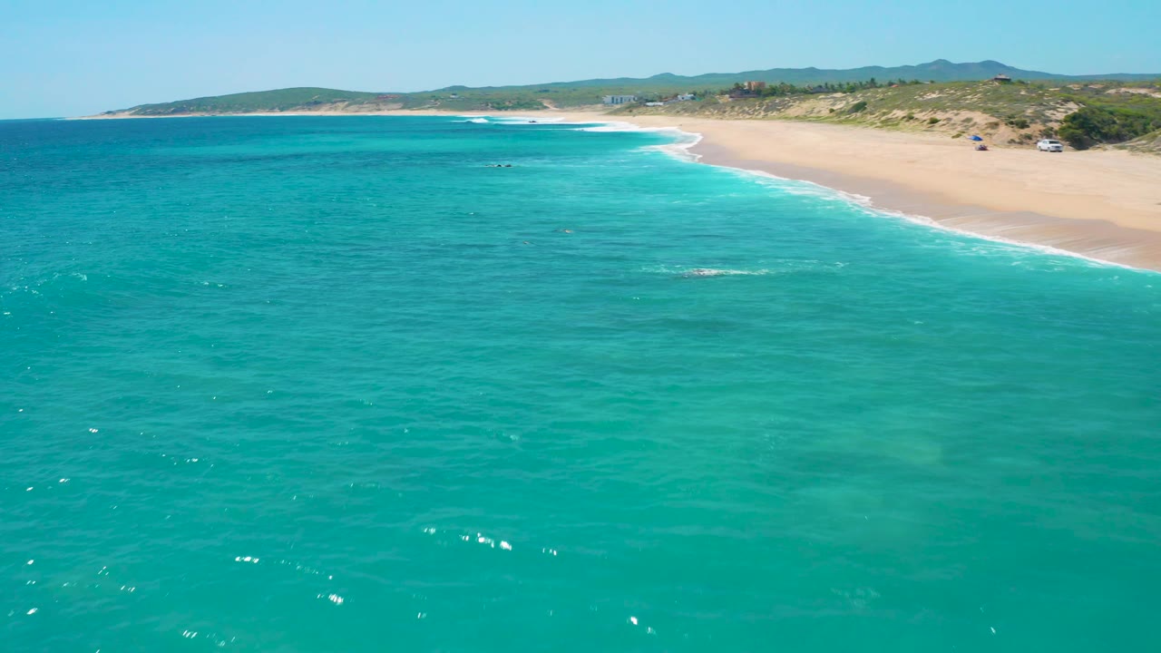 Aerial coastline view with teal water and sandy beach to the right.