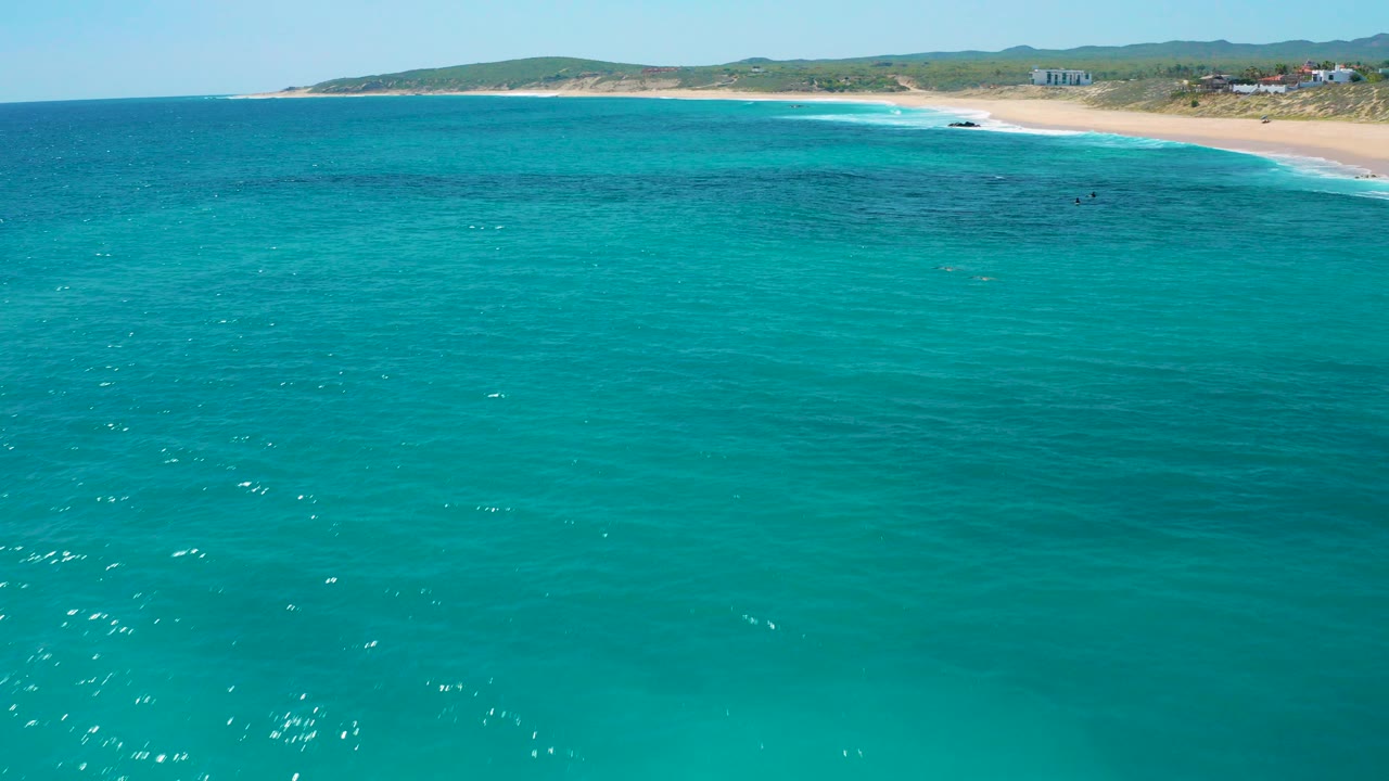 Turquoise sea facing a sandy beach and low hills.
