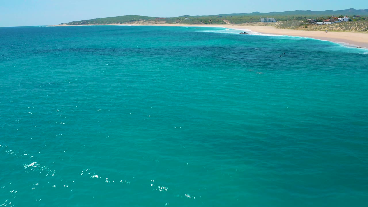 Blue-green sea fills the frame while white surf marks the sandy beach at El Cardoncito in the distance, with no visible people.