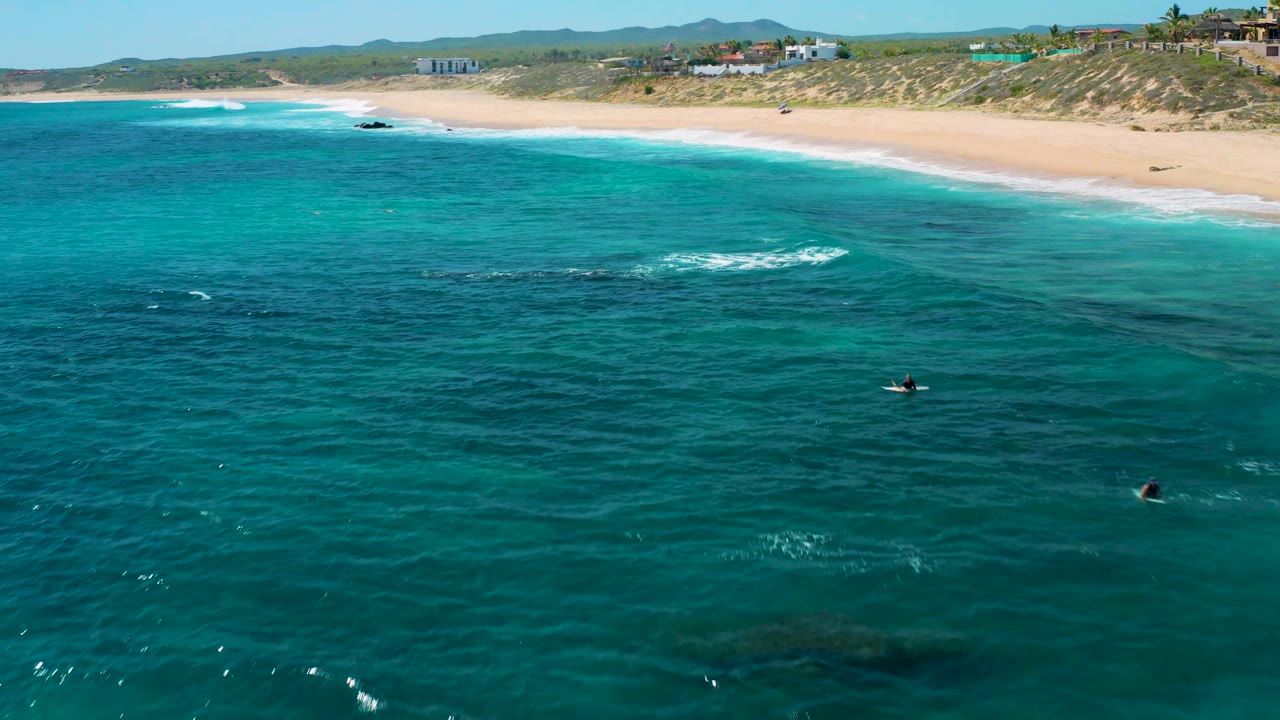 Aerial view of turquoise water and a long sandy beach under clear light.