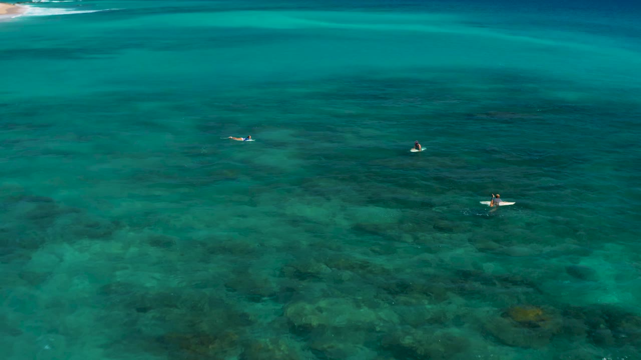Surfers spread across turquoise water with reef texture below.