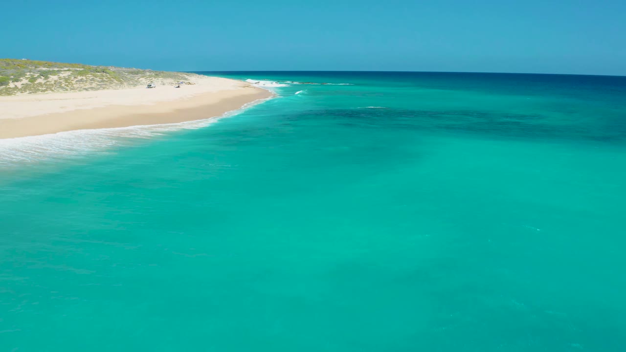 The sea fills the foreground while the pale sandbar and beach curve along the left edge at El Cardoncito, with no visible people on the shore.