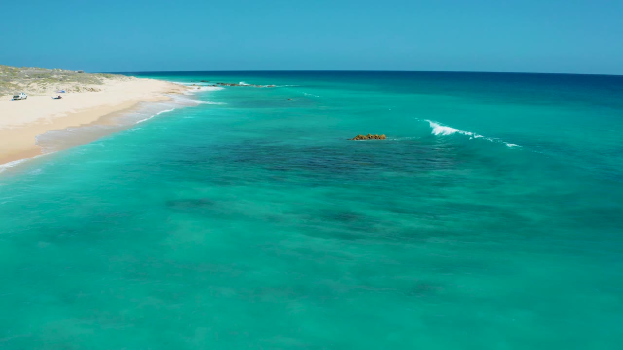 Aerial surf forming near rock patches off a sandy beach.