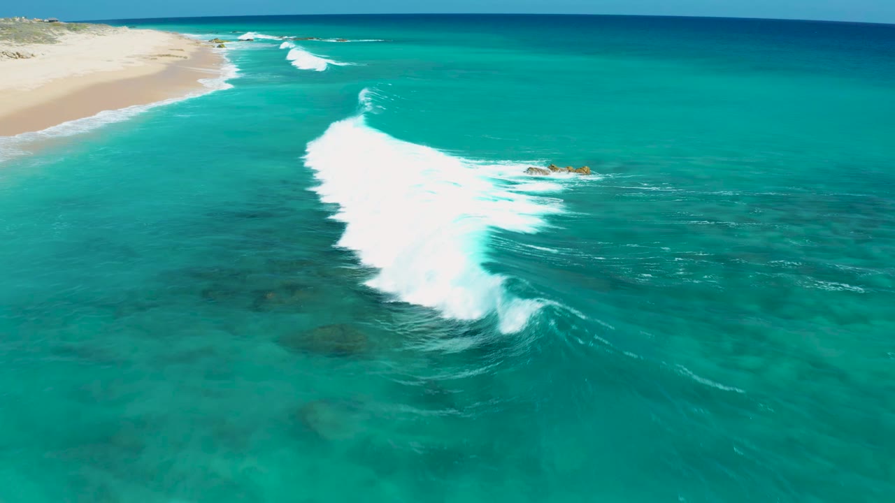 White surf line cutting through turquoise water beside a sandy shore