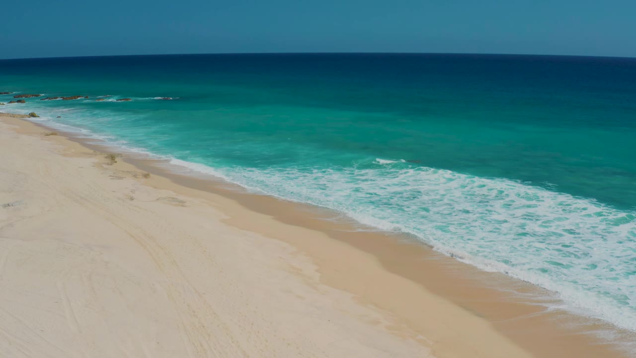 White shore break along a diagonal sandy coastline.